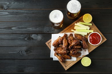 Delicious chicken wings served with beer on black wooden table, flat lay. Space for text