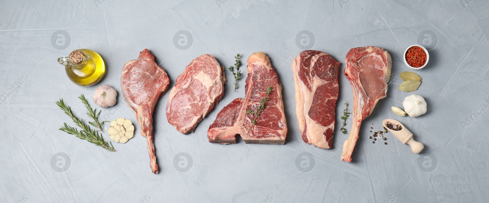 Photo of Fresh raw beef cuts, spices and oil on light grey textured table, flat lay