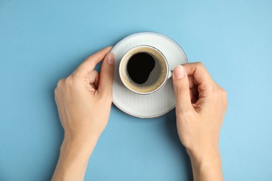 Woman with cup of hot aromatic espresso on light blue background, top view
