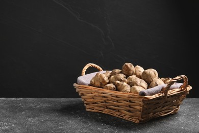 Wicker basket with many Jerusalem artichokes on light grey table, space for text