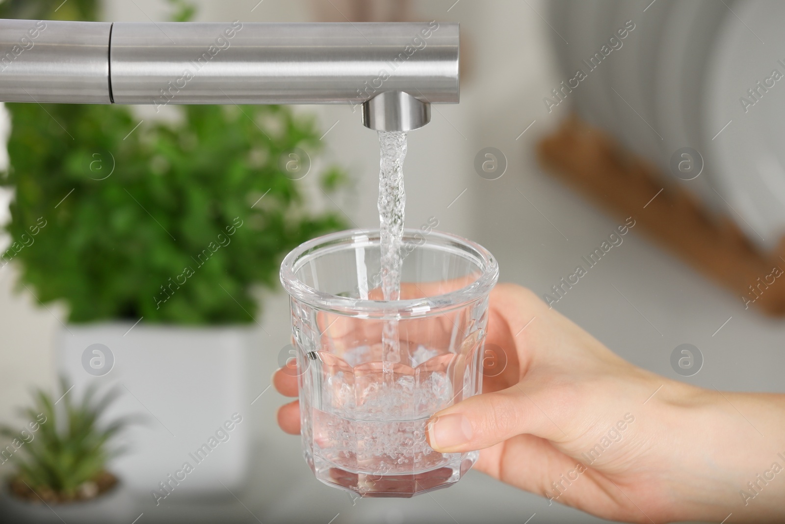 Photo of Woman filling glass with tap water from faucet in kitchen, closeup