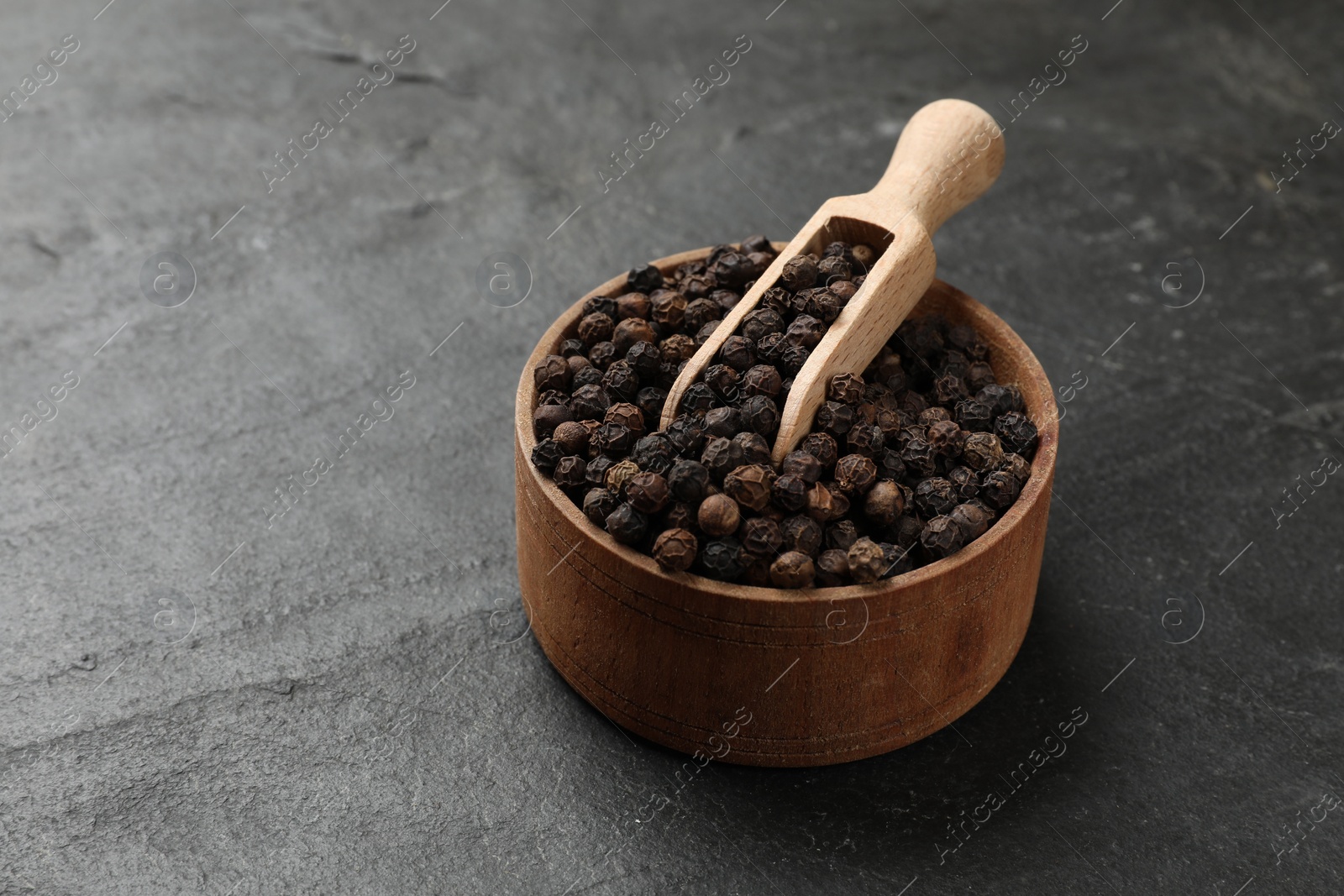 Photo of Aromatic spice. Pepper in bowl and scoop on black table