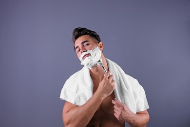 Handsome young man shaving on color background