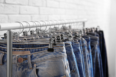 Photo of Rack with stylish jeans near brick wall, closeup