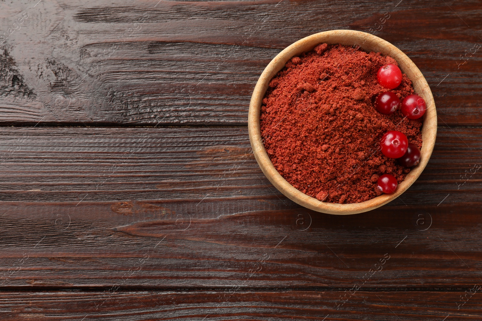 Photo of Dried cranberry powder and fresh berries in bowl on wooden table, top view. Space for text