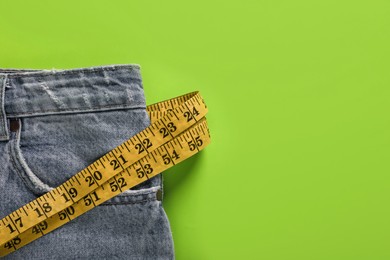 Photo of Jeans and measuring tape on green background, top view with space for text. Weight loss concept