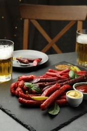 Different thin dry smoked sausages, sauces and glasses of beer on grey table