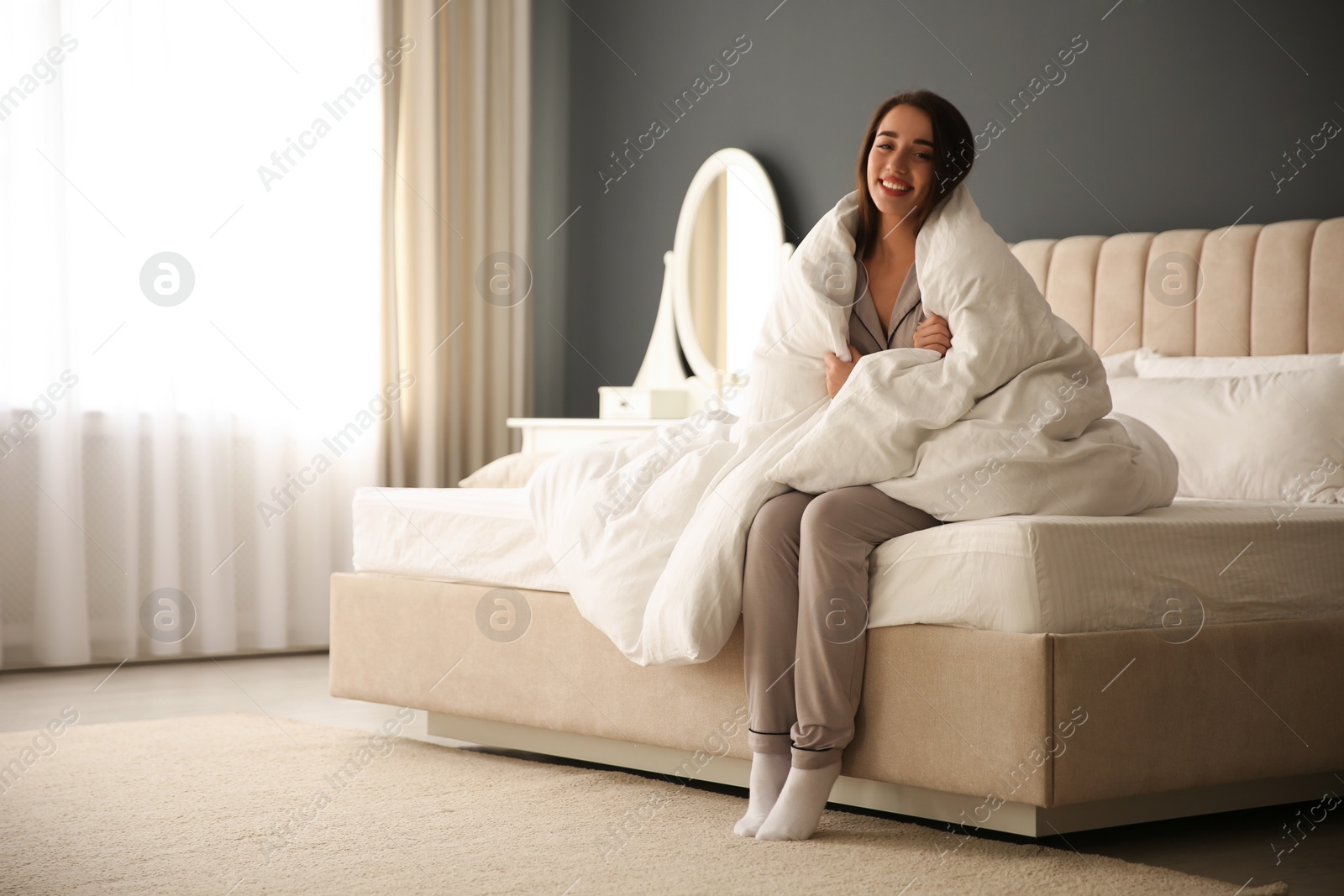 Photo of Beautiful young woman wrapped with soft blanket sitting on bed at home