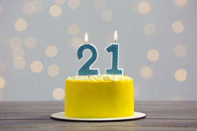 Photo of Coming of age party - 21st birthday. Delicious cake with number shaped candles on wooden table against blurred lights