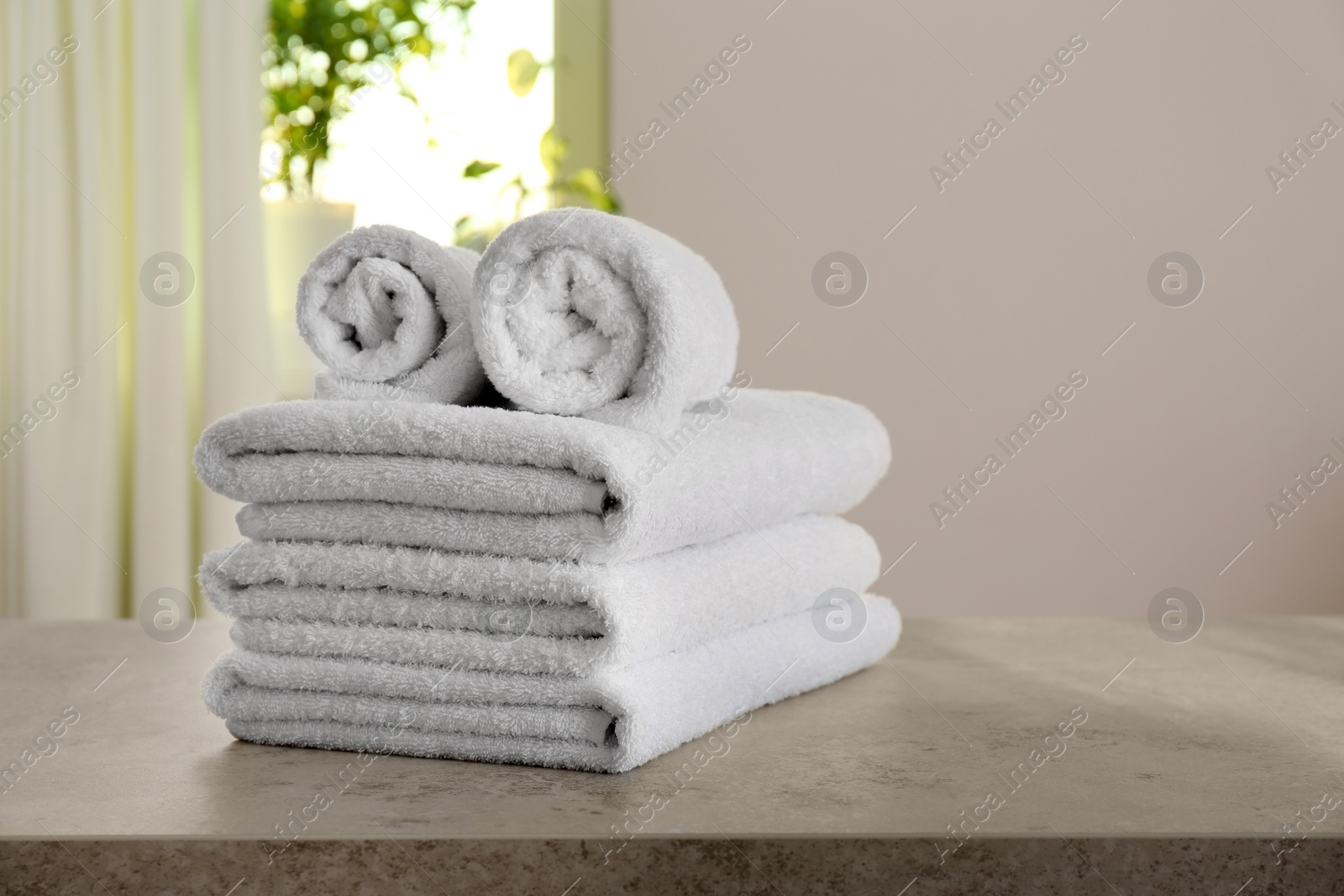 Photo of Stack of fresh towels on light grey stone table in bathroom