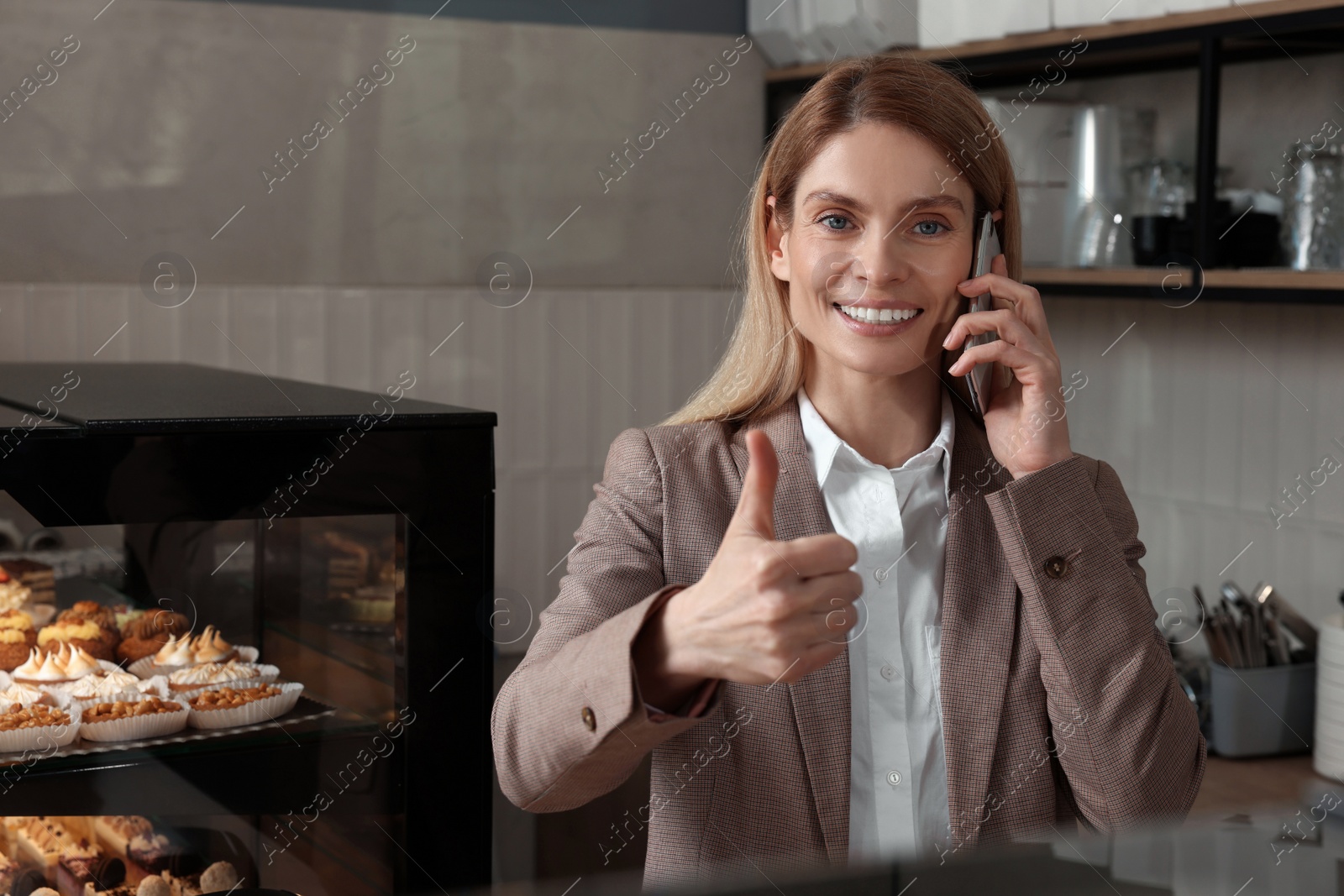 Photo of Happy business owner talking on phone and showing thumb up in bakery shop