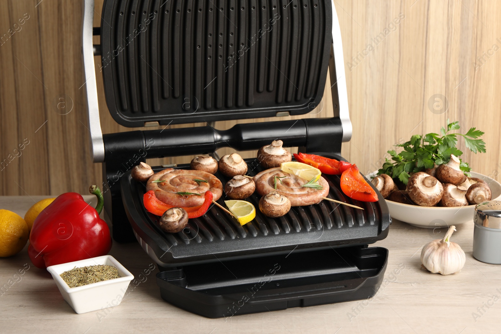 Photo of Electric grill with homemade sausages, vegetables and spices on wooden table