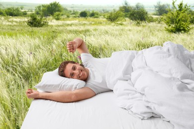 Image of Happy man on bed with soft pillows and beautiful view of green meadow on background. Sleep well - stay healthy