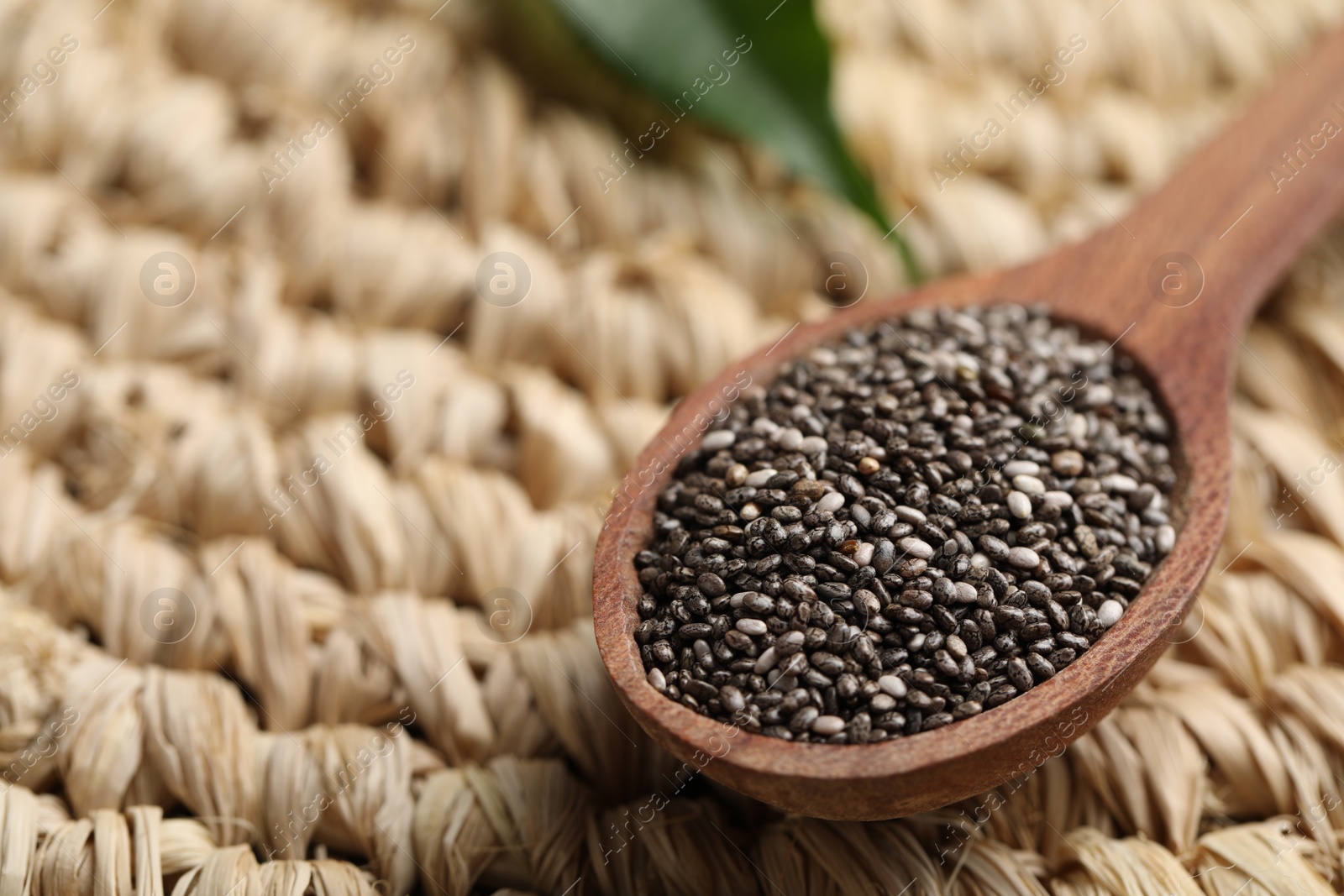 Photo of Wooden spoon with chia seeds on wicker stand, closeup. Space for text