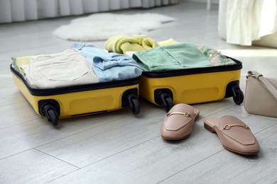 Photo of Open suitcase packed for trip, handbag and shoes on floor indoors