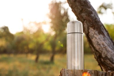 Photo of Modern silver thermos on tree stump outdoors. Space for text
