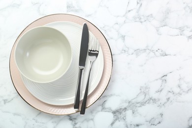 Photo of Clean plates, bowl and cutlery on white marble table, top view. Space for text