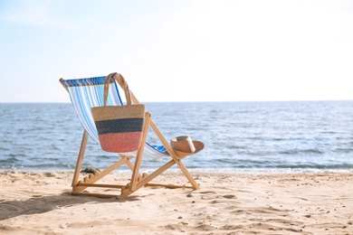 Photo of Lounger, hat and bag on sand near sea, space for text. Beach objects