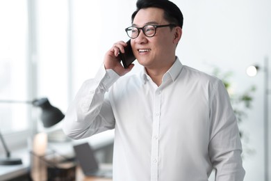Portrait of smiling businessman talking by smartphone in office