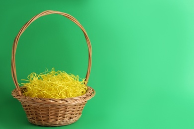 Easter basket with yellow paper filler on green background, space for text