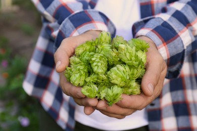 Photo of Man holding fresh green hops outdoors, closeup