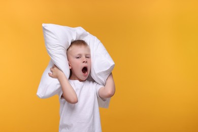 Photo of Sleepy boy with pillow yawning on orange background, space for text. Insomnia problem