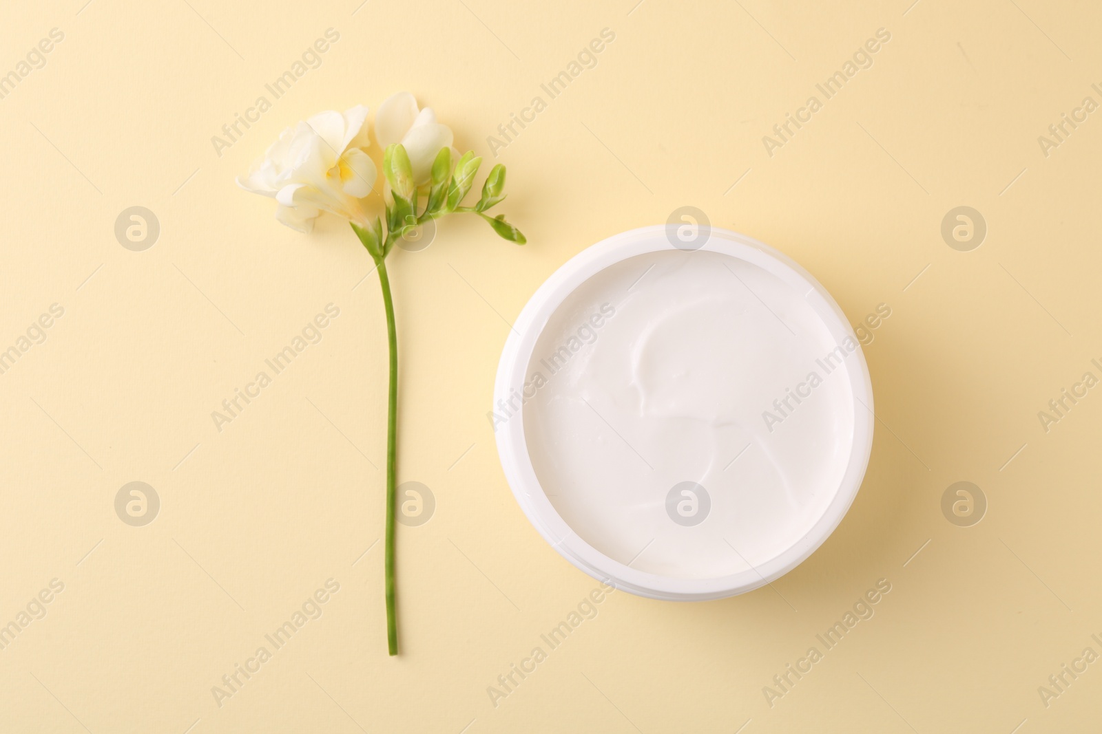 Photo of Moisturizing cream in open jar and freesia flower on beige background, flat lay. Body care product