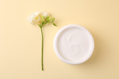 Photo of Moisturizing cream in open jar and freesia flower on beige background, flat lay. Body care product