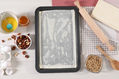 Photo of Making delicious baklava. Baking pan with dough and ingredients on white wooden table, flat lay