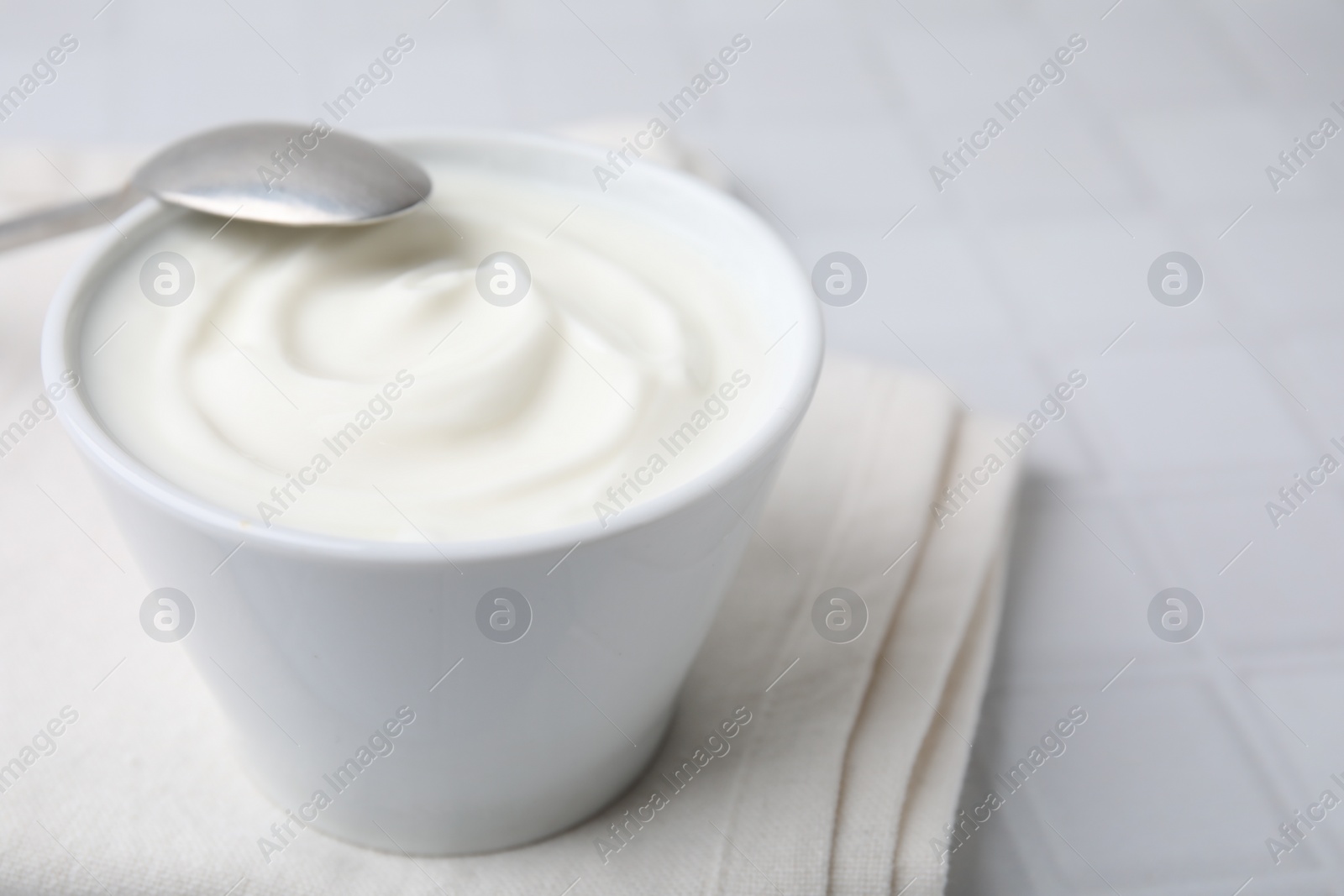 Photo of Delicious natural yogurt in bowl and spoon on white tiled table, closeup. Space for text