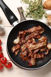 Delicious bacon slices in frying pan and products on light wooden table, flat lay