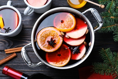 Photo of Delicious mulled wine and ingredients on black wooden table, flat lay