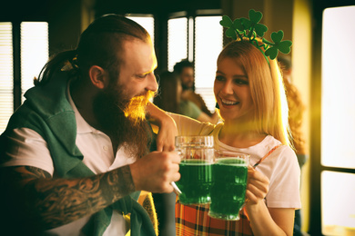Young woman and man toasting with green beer in pub. St. Patrick's Day celebration