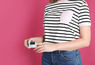 Photo of Young woman checking pulse with digital medical device on color background, closeup. Space for text