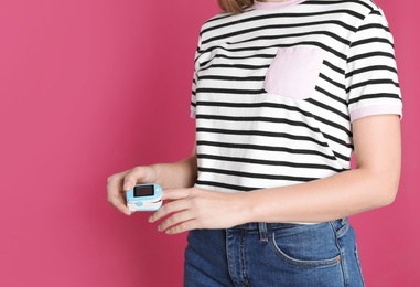 Young woman checking pulse with digital medical device on color background, closeup. Space for text