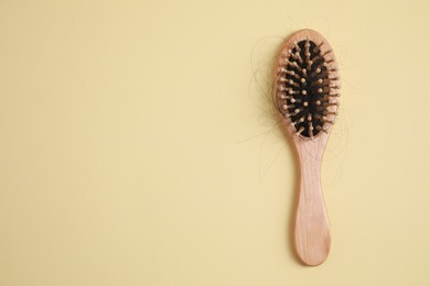 Photo of Wooden brush with lost hair on beige background, top view. Space for text