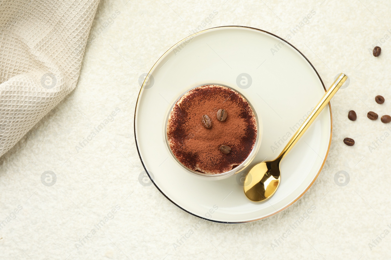 Photo of Delicious tiramisu in glass, coffee beans and spoon on white table, top view