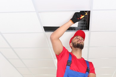 Photo of Electrician with pliers repairing ceiling light indoors, low angle view. Space for text