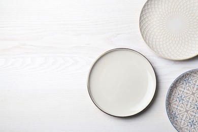 Three beautiful plates on white wooden table, flat lay. Space for text