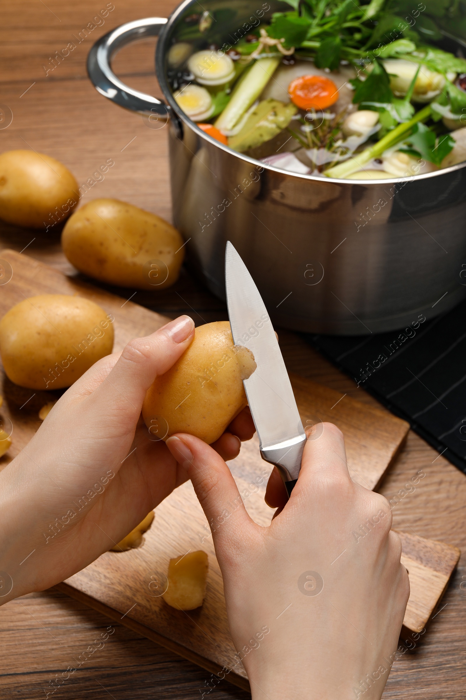 Photo of Woman peeling potato for cooking tasty bouillon at wooden table, closeup