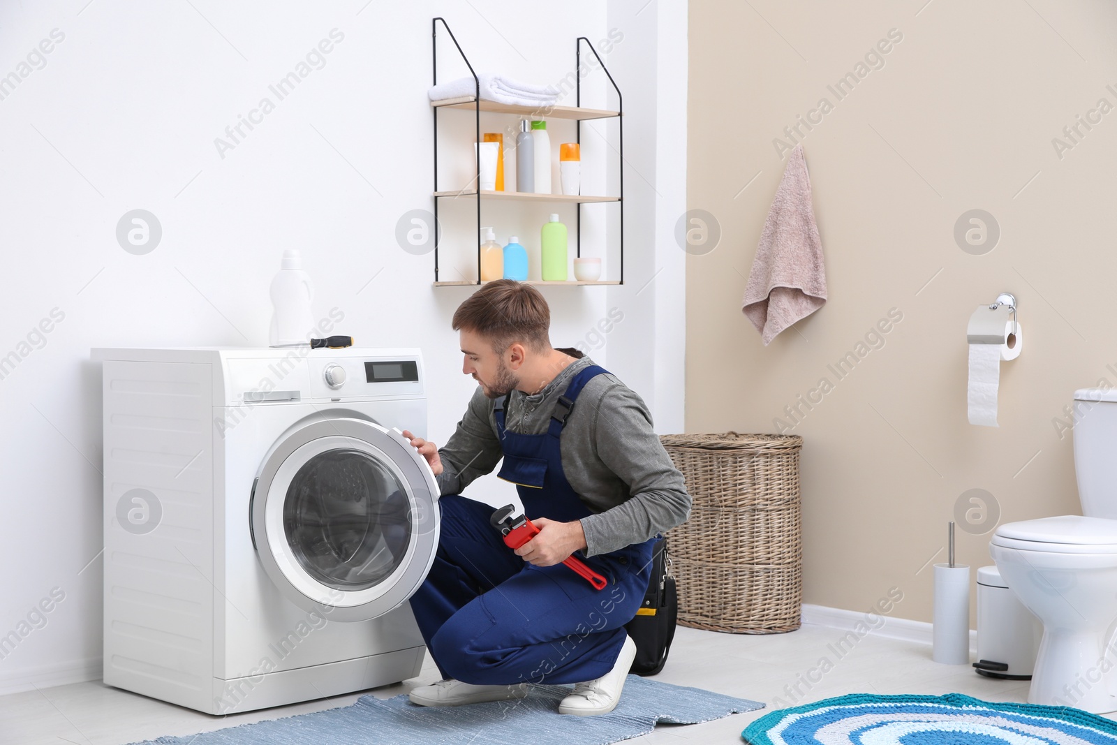 Photo of Young plumber fixing washing machine in bathroom