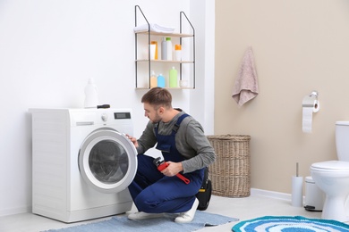 Young plumber fixing washing machine in bathroom