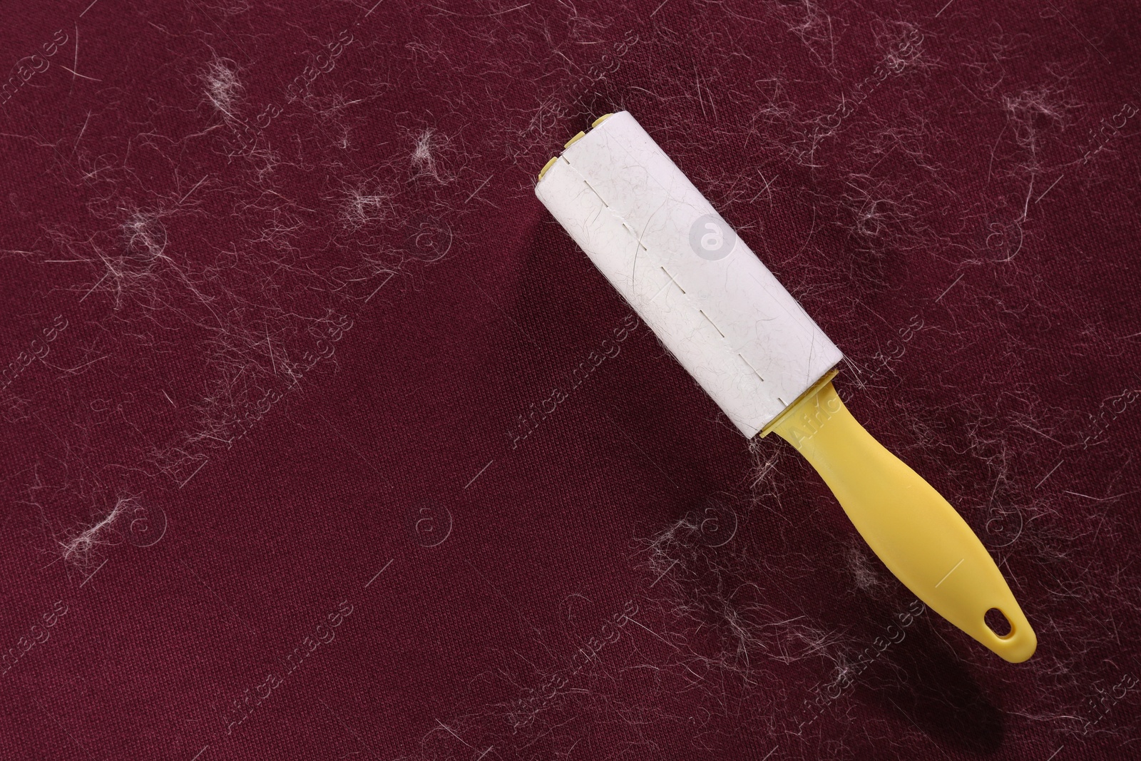 Photo of Lint roller on red fabric covered with hair, top view. Space for text
