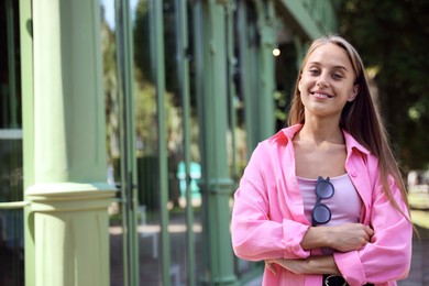 Beautiful young woman with stylish sunglasses near building outdoors, space for text