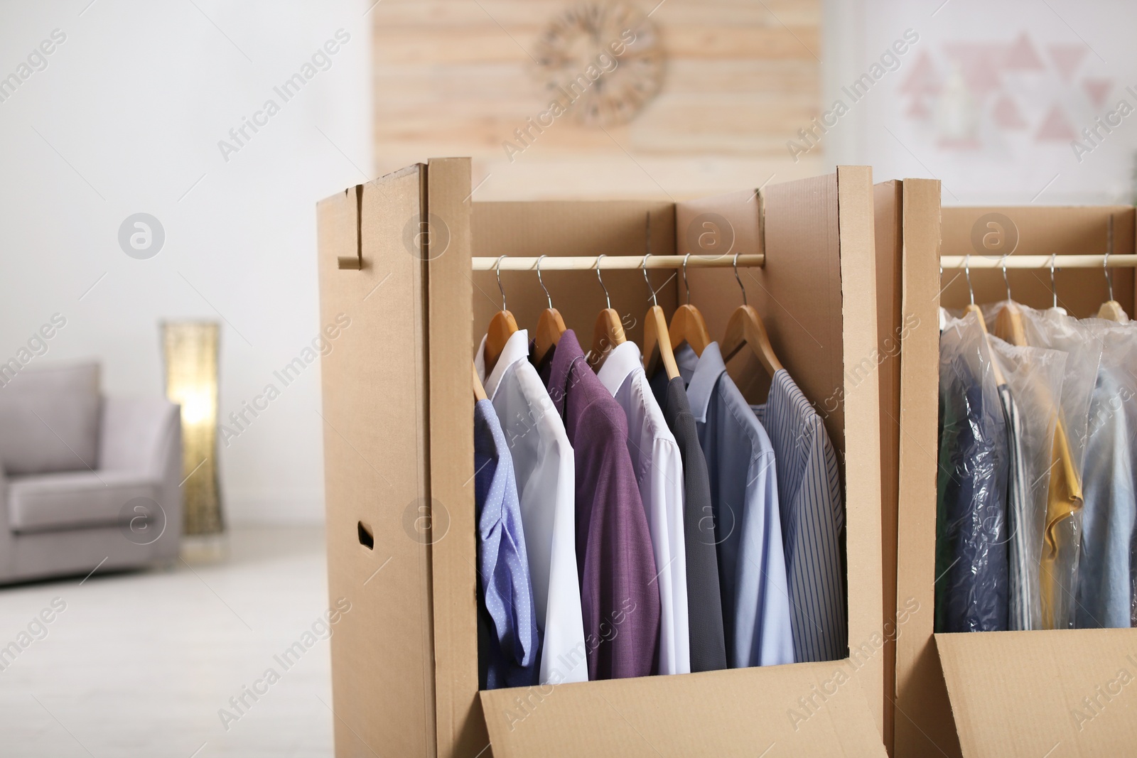 Photo of Cardboard wardrobe boxes with clothes on hangers in living room