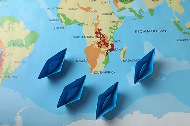 Light blue paper boats on world map, flat lay