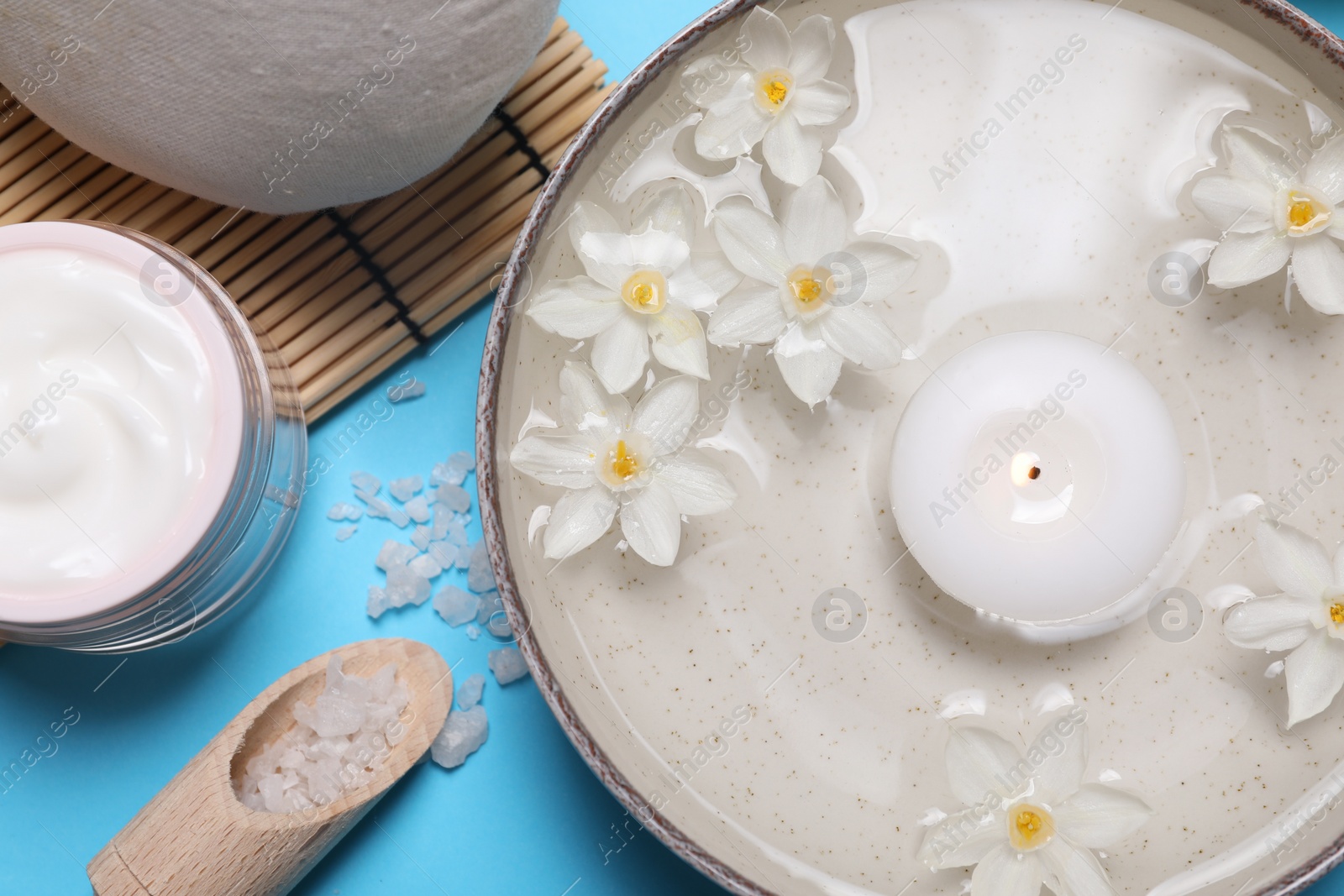 Photo of Beautiful composition with spa products, burning candle and flowers on light blue background, flat lay