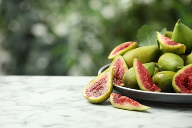 Cut and whole green figs on white marble table against blurred background, space for text