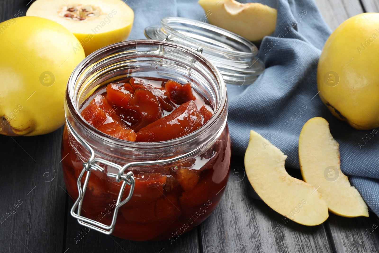 Photo of Quince jam in glass jar and fresh raw fruits on grey wooden table, closeup