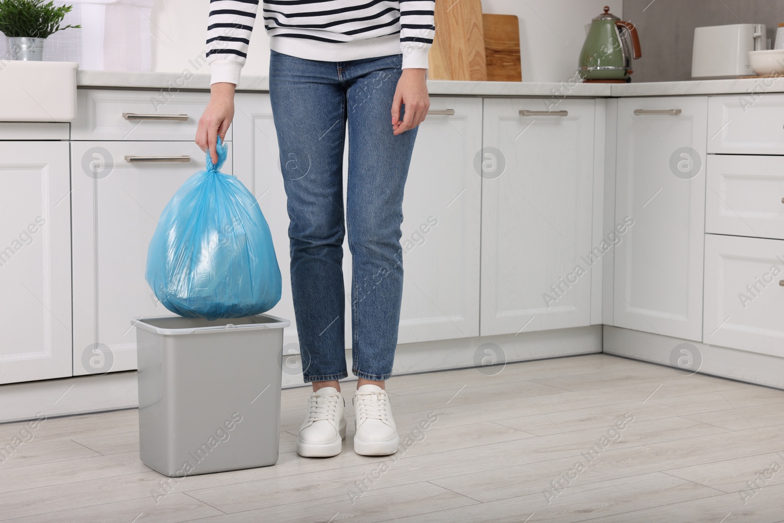 Photo of Woman taking garbage bag out of trash bin in kitchen, closeup. Space for text